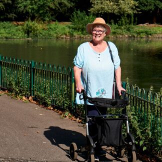 Mujer mayor sonriente paseando con un andador de ruedas junto a un lago