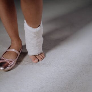 Pie de una niña con escayola junto a una bailarina rosa